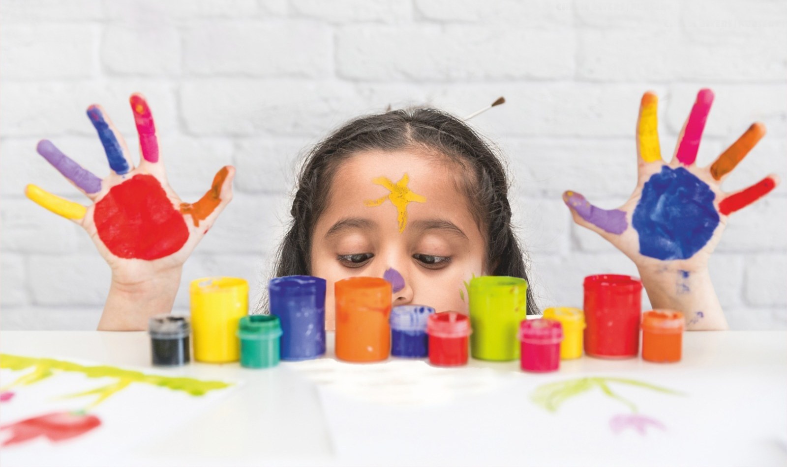 Young girl with colorful painted hands and paint pots at Vedant International Preschool Ahmedabad